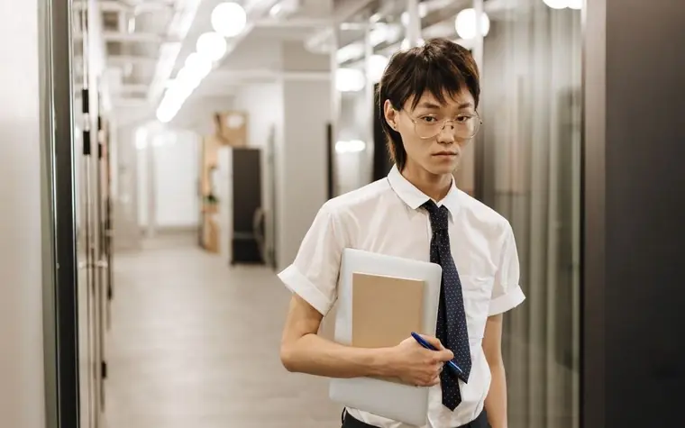 서류를 들고 사무실 복도를 걷는 정장 차림의 사람