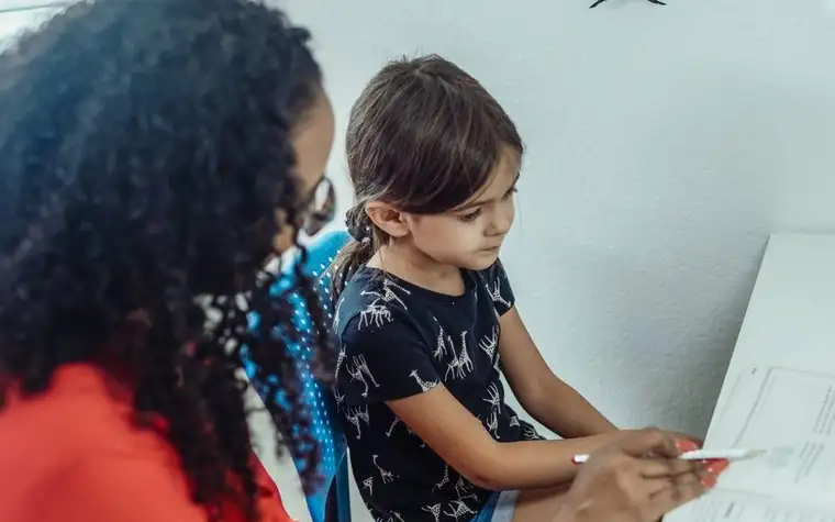 A teacher sitting across from a child, working through something on a screen together