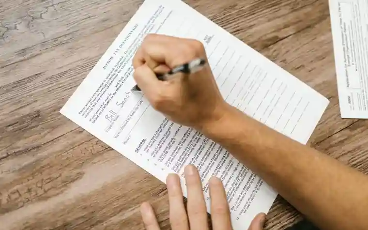 A hand filling in a paper form with a pen